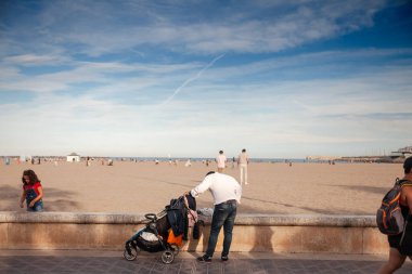 VALENCIA, İspanya - 13 Ekim 2024: Valenciarefefefe İspanyol nüfus, babalık ve aile hayatı İspanyol toplumunda Playa de las Arenas 'ın önünde bebek arabasıyla gezen bir baba.