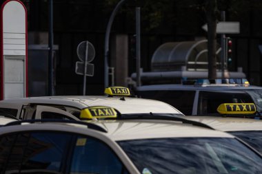 Bir grup Alman taksisinin sembolik sarı çatı tabelaları bir Alman şehrinin ulaşım altyapısını gösteren şehir ortamında dizilmiş..