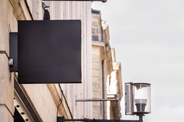 A blank black rectangular shop sign mounted on a building, ideal for branding or store identification in a commercial district. clipart