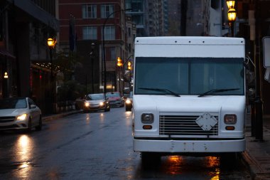 A white delivery van parked on a wet downtown street in North America, reflecting urban logistics and courier services in a rainy evening cityscape. clipart