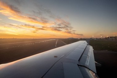 Sırbistan 'ın Belgrad Havaalanı pistinde şafak vakti kalkışa hazırlanan bir uçağın seçici bulanıklığı, rüzgarına odaklanmış ve kalkışa hazır. Altın gökyüzü ve havaalanı ışıklarının manzarası.