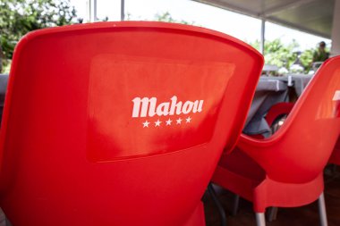 VALENCIA, SPAIN - OCTOBER 13, 2024: Closeup of a Mahou beer logo on a red chair in a bar in Valencia. Mahou san miguel is a spanish beer producer. clipart