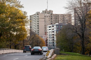 Urban road in Montreal's Cote des Neiges area during autumn, showcasing vehicles passing by with residential buildings in the background. A glimpse into city life in Quebec, Canada. clipart