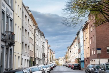 Aachen 'daki banliyö caddesinde çok katlı binalar var. Park halindeki arabalar ve üniforma cepheleri yumuşak gün ışığında tipik bir Batı Avrupa mahallesi sahnesi oluşturuyor..