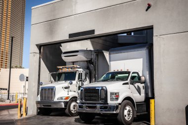 LAS VEGAS - AUGUST 23, 2024: Delivery trucks at a Las Vegas warehouse loading zone managing freight & unloading tasks in this commercial facility, reflecting active shipping and trucking operations. clipart