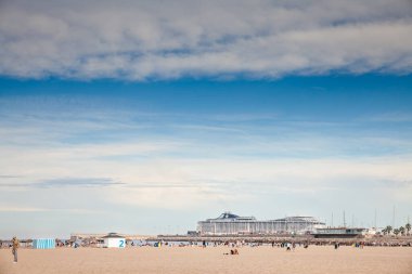 VALENCIA, İspanya - 14 Ekim 2024: Playa de las Arenas, plaja gidenlerin Akdeniz 'deki uzak limanda büyük bir yolcu gemisi olarak kumsalda dinlendikleri sıcak bir gökyüzü altında uzanır..