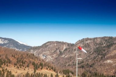 A red windsock stands against the Julian Alps in Bohinj, Slovenia. The alpine valleys rugged slopes form a striking natural backdrop, illustrating local weather conditions in a scenic landscape clipart