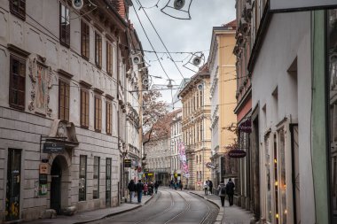 GRAZ, AUSTRIA, 21 ARALIK 2024: Neutorgasse in graz tarihi cepheler, bayram ışıkları ve hafif bir tramvay rotası sunar. Yoldan geçenler bu şehir koridorundaki dükkanları ve kafeleri keşfediyorlar