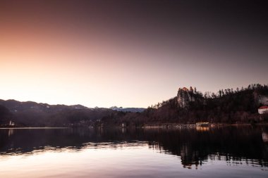 Panorama of the Bled lake, Blejsko Jezero, with its castle, Blejski Hrad, during a winter dusk sunset with the mountains of Julian alps. Bled Castle is a major monument of Slovenia. clipart