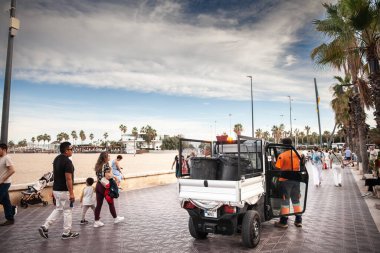 VALENCIA, SPAIN - 13 Ekim 2024: Parlak üniformalı belediye çalışanları Valencias 'ın popüler plaj gezisi boyunca küçük bir çöp kamyonu işleyerek şehrin kamu alanlarını temizleme kararlılığını vurguluyor