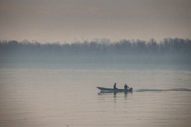 BELGRAD, SERBIA - 12 Ekim 2024: Sırbistan 'ın Belgrad kentindeki Tuna Nehri' nde alacakaranlıkta sürat teknesinde bulunan iki balıkçı, sakin nehir faaliyetlerini ve boş vakitleri yansıtıyor.