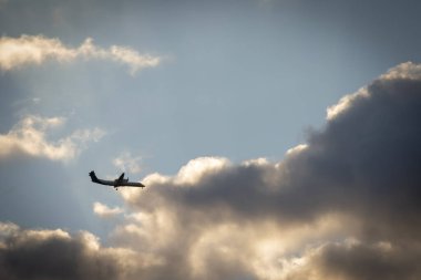 Alacakaranlıkta bulutların arasında uçan bir turboprop uçağı, iniş için hazır, dramatik gökyüzü ve atmosferik aydınlatma ile yakalandı..