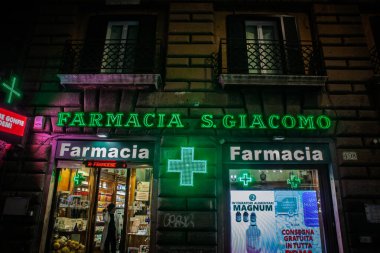 Roma, İtalya - 15 Ocak 2025: Roma 'nın merkezinde yer alan aydınlık İtalyan eczanesi Farmacia S. Giacomo' nun gece görüşü, sağlık hizmeti sembolünü ve eczane penceresini gösteriyor..