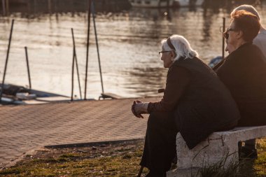 PANCEVO, SERBIA - 16 Mart 2025: Pancevo 'da yaşlı bir Sırp kadın, ömür boyu deneyimi ve kültürel mirası aktaran düşünceli bir şekilde bir bankta oturuyor.
