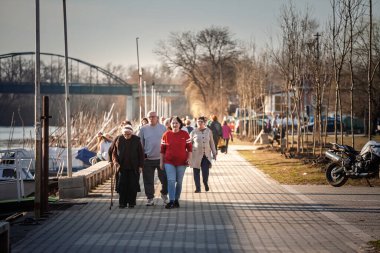 PANCEVO, SERBIA - 22 Mart 2025: Yaşlı sakinler bir öğleden sonra Panevo 'daki Tamis nehrinin kıyısında yürüyüş yaparak, nehir kenarındaki yolu egzersiz, sohbet ve suyun yanında toplum hayatı için kullandılar.
