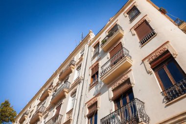 Valencia Eixample 'da 19. yüzyılın sonlarında güneş ışığı altında kalan apartman bloğu: süslü sıva işleri, sargı bezleri, balkonlar ve krem cepheleri İspanya' daki emlak ve mülkiyetin bir sembolü olan gökyüzüne yükseliyor.