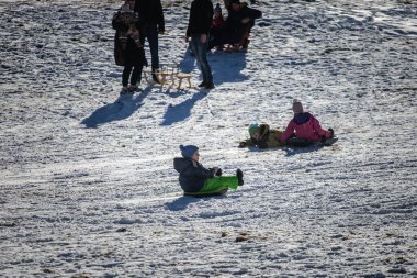 ZGORNJE JEZERSKO, SLOVENIA - 23 Aralık 2024: Çocuklar kızaklarla tepe aşağı inerken, aileler Slovenya 'nın Zgornje Jezersko kentindeki kar kaplı bir yamaçta eğlendirici kış oyunlarını izliyorlar