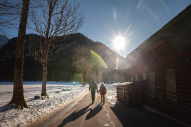 ZGORNJE JEZERSKO, SLOVENIA - 23 Aralık 2024: Gün batımında donmuş Jezersko Gölü 'nün yanında yürürken uzun gölgeler, karlı Alp yolunu aydınlatan lensler.
