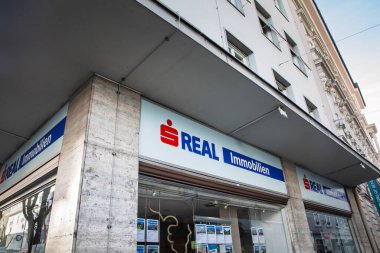 KLAGENFURT, AUSTRIA - 17 Aralık 2024: Sparkasse Group 'un (Erste Grubu) bir parçası olan S Real Immobilien logosu bir emlak bürosu köşesine hükmediyor; mülkiyet listeleri pencereyi dolduruyor.