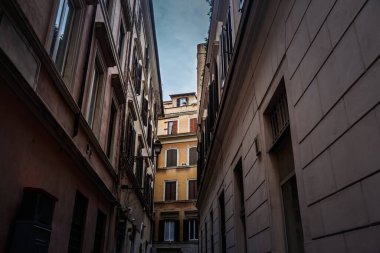 Uzun panjurlu gölgelerle çevrili loş, dar bir sokağa bakarken manzara, eski Roma 'nın Sonsuz Şehri' nin göbeğinde yükselen güneşli dairelerde sona erer.