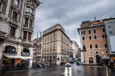 ROME, ITALY - 15 Ocak 2025: Slick asfalt, Centro Storico yakınlarındaki bir öğleden sonra duşunda şemsiyelerin, scooterların ve kafelerin kavşağı canlandırdığı Piazza Barberini 'deki Barok cephelerini yansıtıyor.