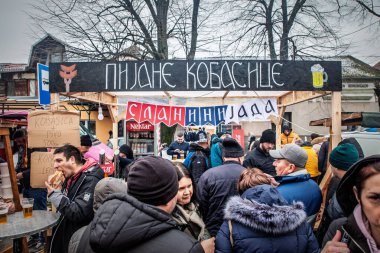 KACAREVO, SERBIA - 13 Şubat 2025: Slaninijada pastırma pazarı sırasında Srunk Sausages Bar 'da kuyrukta bekleyenler, Kacarevo' da Kiril alfabesinde ızgara atıştırmalık bira içenler.