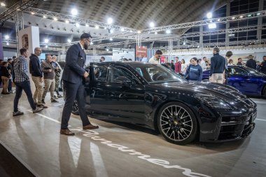 BELGRAD, SERBIA - 15 Mart 2025: uygun bir satış temsilcisi, siyah bir Porsche Panamera 'nın kapısını açıyor ilgili ziyaretçiler kalabalıklaşırken. Porsche bir Alman otomobil üreticisi.