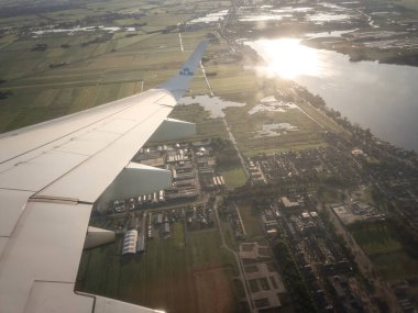AMSTERDAM, NETHERLANDS - 21 AĞUSTUSTOS 2024: Hollanda banliyösü üzerinde, bir KLM uçağı kanalların, polder alanlarının ve sabah bir kasabanın üzerinde uzanır, Amsterdam yakınlarındaki bir Hollanda manzarasının havadan görüntüsü