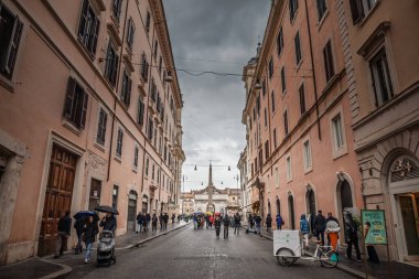 ROMA, İtalya - 15 Ocak 2025: Flaminio Obelisk kara kara kara düşünen bulutların altında ilerlerken Via del corso tarafından Piazza del Popolo 'ya doğru hareket eden şemsiyeli yayalar. Del Corso üzerinden Roma ana caddesi.