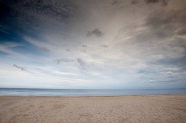 Jurmala, Dubulti, Letonya 'da dramatik bulutlar altında boş bir Baltık plajının engin deniz manzarası. Pürüzsüz su ve el değmemiş kum minimalist bir ufuk oluşturur, yalnızlığı ve kıyı atmosferini taşır..
