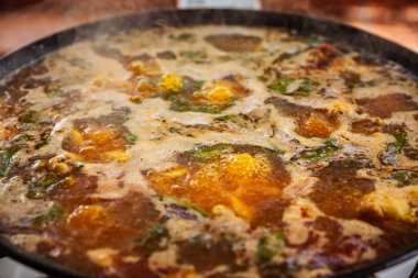 Geleneksel Valensiyalı paella 'nın (paella valenciana) geniş bir tavada fokurdaması yakından görülüyor: safran çorbası, tavuk, tavşan, yeşil fasulye birlikte kaynıyor, köpükler yavaş emilimi işaret ediyor