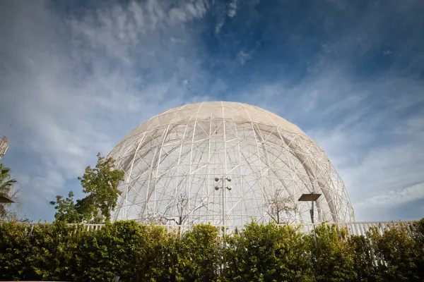 VALENCIA, İSPA - 13 Ekim 2024: Bioparc Valencia 'daki geniş kafes kubbesi, açık Akdeniz gökyüzüne karşı yemyeşil yemyeşil bir yeşil alandan yükseliyor, egzotik kuşları çevreleyen beyaz çelik iskeleti.