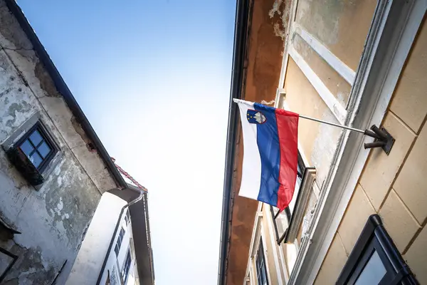 Slovenya 'nın kırmızı-beyaz-mavi bayrağı ortaçağ Skofja Loka, Slovenya' sındaki eski bir evden dalgalanmakta, açık bir alp gökyüzüne ve yaşlanmakta olan alçı cephelerine karşı üç rengi parlıyor.