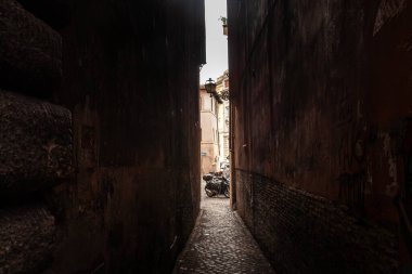 Roma, İtalya - 15 Ocak 2025: Bir çift scooter Roma 'nın tarihi merkezinde loş, dar bir caddenin ağzında bekler; kaldırım döşeme taş duvarlar parlak ötesine doğru dar bir koridor oluşturur.