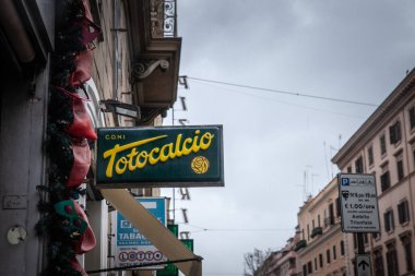 ROME, İtalya - 15 Ocak 2025: Yağmurlu bir öğleden sonra Roma 'daki bir bahis dükkanının önünde asılı Totocalcio neon tabelası; yeşil panel, sarı harf ve futbol logosu.