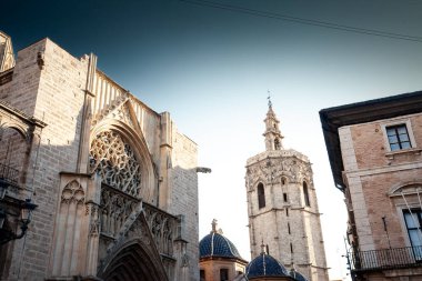 Valencia Katedrali 'nin gotik cephesinde akşam gökyüzünün altındaki Micalet çan kulesinin yanında süslü bir gül penceresi yükseliyor ve eski şehrin ufuk çizgisini şekillendiren tarihi mimariyi vurguluyor.