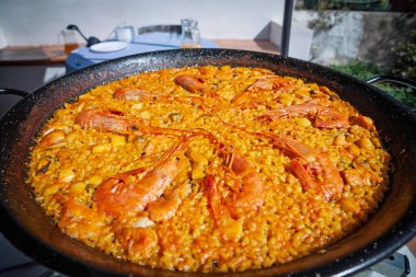 Siyah tavada geleneksel Valensiyalı deniz ürünleri paella 'sının (paella de mariscos) yakın plan görüntüsü; midyeli safran pilavı ve açık havada yapılan bir yemek sırasında tam karides..
