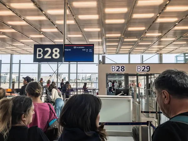 PARIS, FRANCE - 26 AĞUSTOS 2024: Charles de Gaulle Havaalanı 'nın JU241 sefer sayılı Air Serbia uçağı için B28 numaralı kapısında kuyruğa giren yolcular, kalkış ekranları ve havayolu, kapı ve istikamet işaretleriyle.