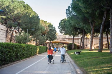 VALENCIA, İspanya - 15 Nisan 2025: Genç ebeveynler İspanya ve İspanya 'daki gençliği resmeden Valencia' nın Jardin del Turia 'sının ağaç çizgili yolu boyunca bebek arabalarını ittiler.