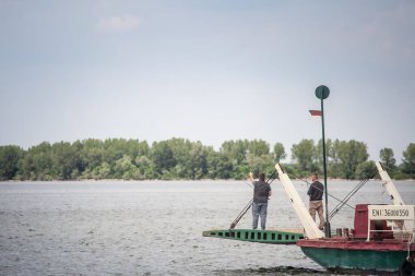 RAM, SERBIA - 15 Mayıs 2025: Tuna nehrinde Ram, Sırbistan 'da demir kapılarında, ilkbaharda bir feribotta balık tutan iki balıkçının seçici bulanıklığı.
