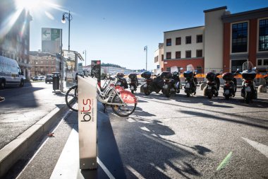 TRIESTE, ITALY - 17 Aralık 2024: Trieste, İtalya 'da BITS bisiklet paylaşım limanı; Adriyatik sahil cephesinde mikro-hareketlilik seçeneklerini vurgulayan, park halindeki scooterların yanında gümüş şehir bisikletleri bekliyor.