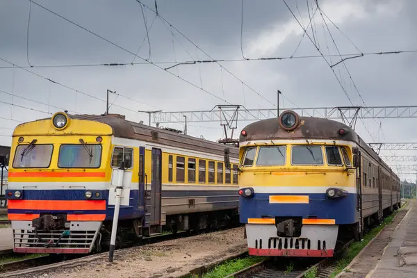 Letonya Demiryolları 'nın iki eski Sovyet tarzı elektrikli çoklu tren Riga Merkez İstasyonu' nda yan yana durur. Letonya, üstteki katenareri kablolarından oluşan bir kafesin altında yolculuklarına başlamaya hazırdır..