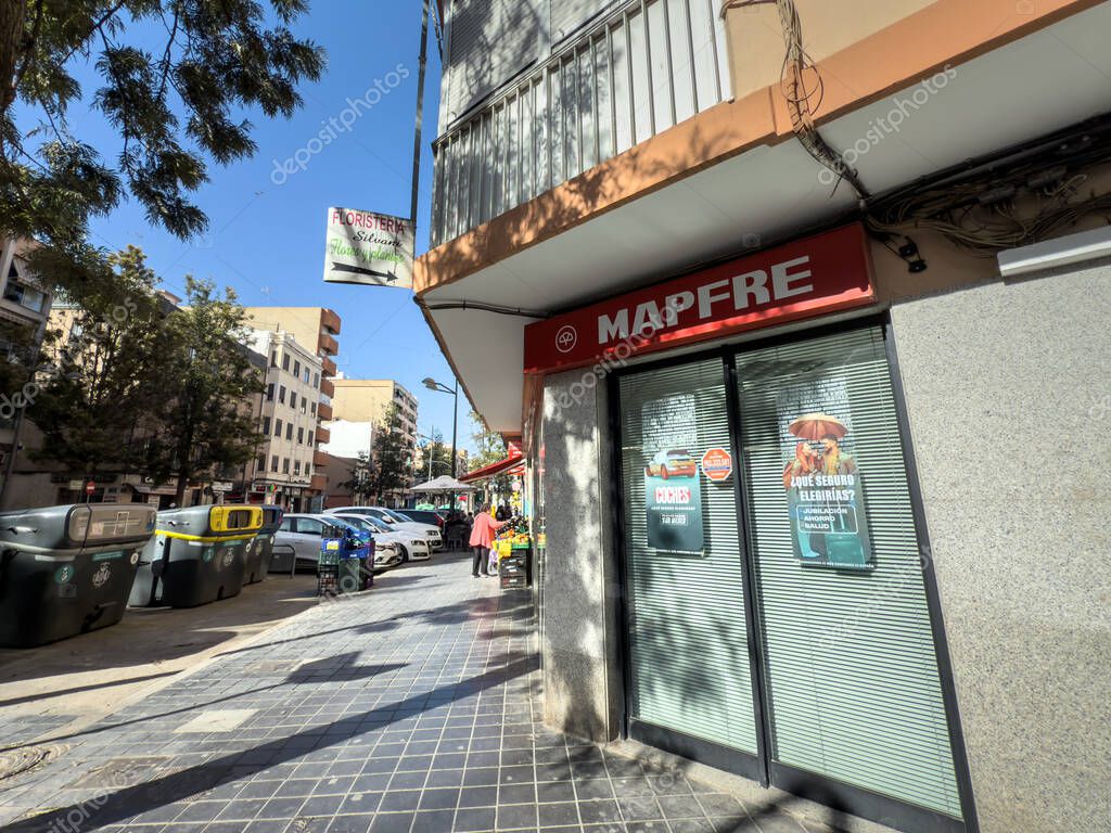 VALENCIA, SPAIN - APRIL 15, 2025: The red Mapfre logo crowns a glass-front branch on a sunny Valencia street. Mapfre is a Spanish insurer specialized in life and non life insurance.