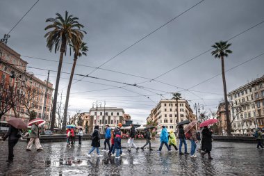 ROMA, İtalya - 15 OCAK 2025: Renkli şemsiyeli yayalar Roma 'nın Piazza del Risorgimento' sunu yağmurda, palmiye ağaçları ve tramvay telleriyle geçerek Umbertino apartmanlarını kara kara kara bulutlar altında çerçevelemektedir..