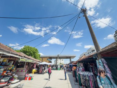 VALJEVO, SERBIA - 22 Mayıs 2025: Yeşil marketin açık hava tezgahları Valthe Zelena Pijaca. Tedarikçiler parlak elbiseler sunuyor, alışveriş yapanlar kiremitli çatılar ve mavi yaz gökyüzü arasında gezinirken.