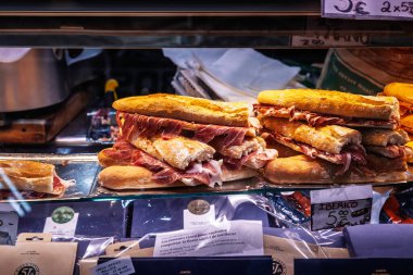 BARCELONA, SPAIN - 12 Nisan 2025: Ekmek üzerine jamon Iberico sandviçleri istiflenmiş açık büfe, Barselona pazarında İspanyol pişirilmiş jambon geleneği ve gurme atıştırmalık kültürü sergileniyor.