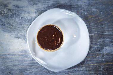 Beyaz bir tabakta, tartelette au chocolat adı verilen mavi ahşap masa üzerindeki tek bir Fransız tartletinin yukarıdan görünüşü Fransız pastanesindeki tipik bir yemektir..