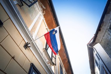 Slovenya bayrağı, Skofja Loka 'daki yıpranmış bir evden gelen üç renkli dalgalar, açık alp gökyüzüne karşı kırmızı beyaz ve mavi parıltı.