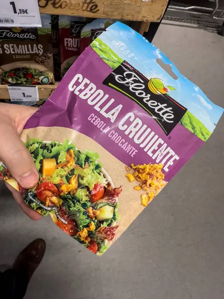 VALENCIA, İSPAIN - 15 Nisan 2025: 'Cebolla Crujiente' markalı Florette marka kızarmış soğan paketini Valencia süpermarketinde yakın çekim. Florette salata konusunda uzmanlaşmış bir Fransız markası.