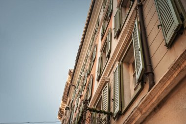 Trieste 'nin eski kenti İtalya' daki pastel cephede üst düzey açık yeşil ahşap panjurlar, süslü balkon demirleri çelenklerle süslenmiş ve sıcak akşam ışığı tarafından aydınlatılan temiz gökyüzü manzarası..